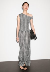 Robe longue à rayures, à une épaule, en noir et blanc. Tissu doux et texturé avec un corsage ajusté et une jupe fluide. Accents de sac à main noir.