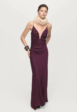 Long, form-fitting plum dress with a deep V-neck and a keyhole detail, paired with a light faux fur collar and chunky black bracelets.