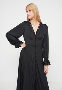 Black long-sleeve dress with a deep V-neck, button-down front, and lace trim detailing on sleeves. Smooth fabric with a flowing silhouette.