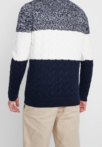 Marinblå och vit kabelstickad tröja med ett strukturerat mönster, ribbade ärmslut och kant, med en enfärgad marinblå nedre del.