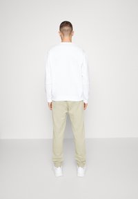 Vit sweatshirt med ribbade ärmar och nederkant, tillsammans med ljusbeige sweatpants. Outfiten fulländas med vita sneakers.