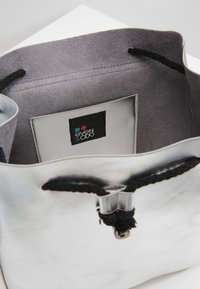 Sac en cuir argenté avec poignées en corde noire et fermoir métallique. Intérieur avec doublure grise douce et étiquette logo. Design simple et minimaliste.