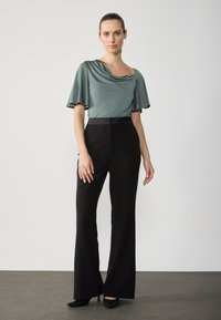 Top drapat de culoare verde ardezie cu mâneci largi, asortat cu pantaloni negri evazați, cu talie înaltă. Modelul poartă tocuri negre; textură de țesătură netedă.