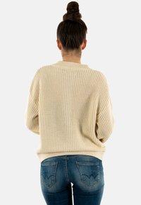 Maglione beige in maglia con vestibilità rilassata e motivo a coste, abbinato a jeans blu lavaggio medio con tasche posteriori curve.