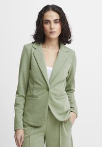 Light green blazer made of textured fabric, featuring a single button closure, two front pockets, and traditional lapels.