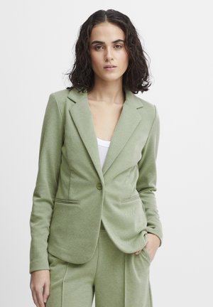 Světle zelený blazer vyrobený z texturované látky, s jedním knoflíkem na zapínání, dvěma předními kapsami a tradičními klopami.