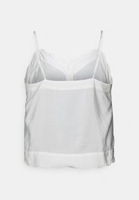 Vit camisole med justerbara spaghetti-axelband, vågig nederkant och lätt, texturerad tyg. Enkelt och minimalistiskt design.