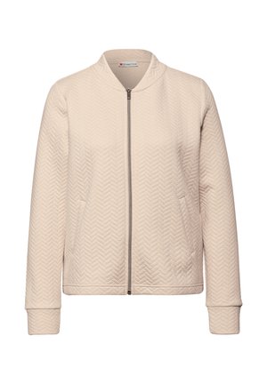 Blouson aviateur matelassé beige clair avec un motif chevrons texturé, fermeture éclair sur le devant et poignets côtelés. Aucune pièce métallique visible.