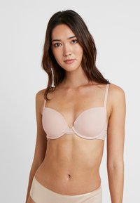 Soutien-gorge rembourré en tissu nude doux avec bretelles ajustables, présentant une finition lisse et un design léger. Armature structurée pour le soutien.