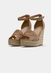 Sandales compensées beiges avec plateforme en jute tressé, des brides croisées sur les orteils et des sangles à la cheville avec des fermetures à boucle en argent.
