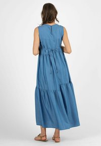 Abito longuette in denim con scollatura rotonda, senza maniche, vita elasticizzata e gonna a strati. Presenta un'apertura sul retro con bottoni e lacci.