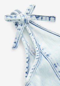Ljus denim bikiniöverdel med knuten rem, ljusblå färg, distinkta sömmar och ett tie-dye-mönster med mörkare blå accenter.