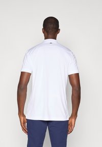 Hvit kortermet skjorte med krage, glatt tekstur, og en liten logo på baksiden. En strømlinjeformet passform passer godt til marineblå bukser.