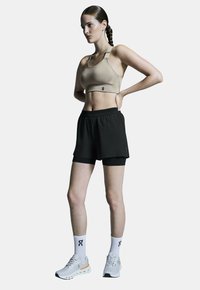 Beige sportbeha en zwarte shorts, met een gladde textuur, elastische tailleband en gelaagd design. Draagt witte sokken en sneakers.