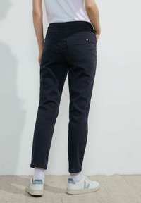 Pantalones de color azul marino con una cinturilla elástica, piernas ajustadas y dos bolsillos traseros. Combinados con zapatillas blancas que tienen un acento en azul claro.