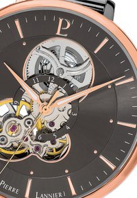 Reloj mecánico con esfera negra, fondo de cristal transparente que revela los mecanismos internos, acentos en oro rosa, manecillas plateadas y marcadores numéricos.