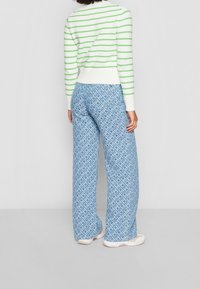 Niebieskie, szerokie spodnie z wzorem w teksturę. Połączone z białym i zielonym swetrem w paski, z prążkowanymi mankietami i dołem.