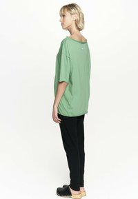 Zielona, oversize t-shirt z krótkimi rękawami, okrągłym dekoltem i luźnym krojem, zestawiony z czarnymi zwężanymi spodniami i chodakami.