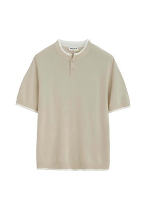 Chemise en maille beige à manches courtes avec patte à deux boutons et col et poignets côtes, superposée à un sous-maillot blanc.