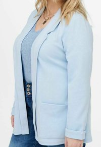 Light blue blazer made of textured fabric. Features a single pocket, rolled cuffs, and an open front design. Paired with a light blue top.