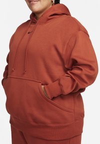 Hoodie couleur rouille avec poche avant, capuche à cordon de serrage et poignets côtelés, fabriqué en tissu doux avec une coupe décontractée. Accent logo noir.