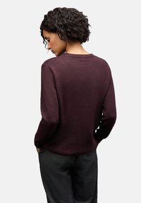 Maglione bordeaux con scollatura rotonda a costine, maniche lunghe e lavorazione a maglia texturizzata. Abbinato a pantaloni grigio scuro, visto da dietro.
