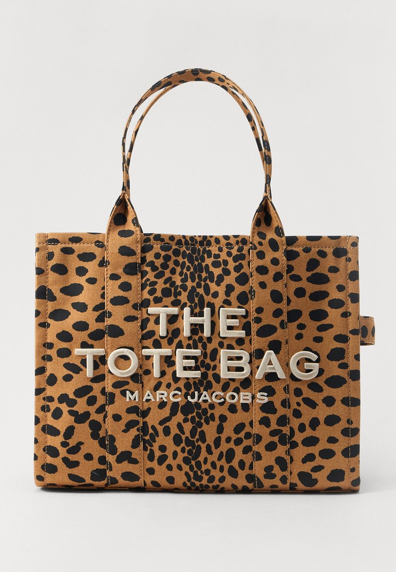 Borsa a mano a macchie marroni e nere con due manici e "THE TOTE BAG MARC JACOBS" ricamato in bianco sul davanti.