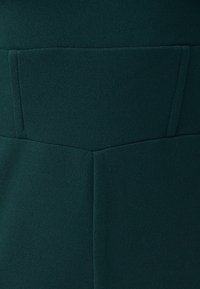 Tmavě zelená látka s hladkým, texturovaným povrchem a strukturovaným designem, včetně obdélníkové kapsy na zadní straně.