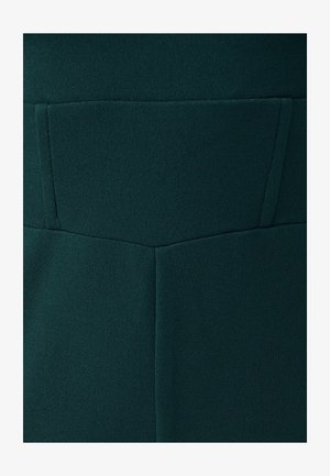 Tamsiai žalia medžiaga, turinti lygią, tekstūruotą paviršių su struktūriniu dizainu, įskaitant stačiakampio formos kišenės detalę gale.