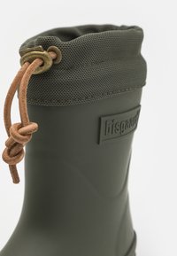 Botte en caoutchouc vert foncé avec un haut en maille texturée, dotée d'un cordon en cuir et d'un logo de marque en relief sur le côté.