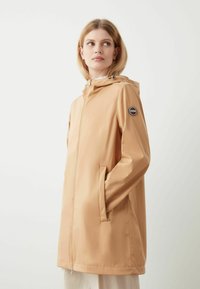Beige wasserdichte Jacke mit Kapuze, einem Frontreißverschluss, zwei Seitentaschen und einem runden Logo-Patch auf dem linken Ärmel. Glatte Textur.