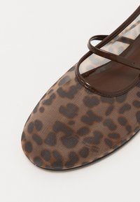 Scarpa piatta con stampa leopardata marrone e nera, superiore in tessuto texture, punta arrotondata e cinghie decorative incrociate sul collo del piede.