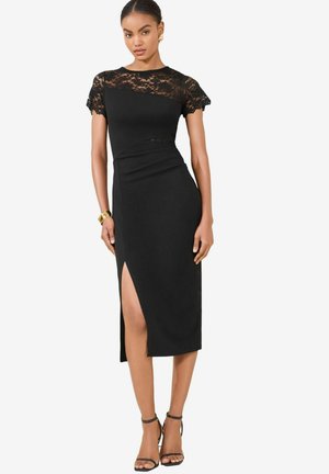 Black dress with a lace top, short sleeves, and a fitted waist. Features a side slit and smooth texture. Worn with strappy black heels.