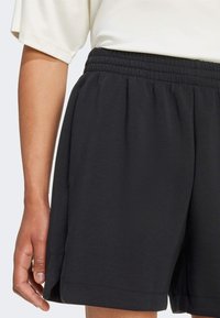 Černé šortky s elastickým pasem, měkkou látkou a bočními kapsami; mají volný, pohodlný střih s jemnými bočními rozparky.