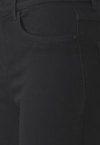 Mustat denimin farkut, joissa lähikuva kangasrakenteesta, näkyvistä saumoista ja sivutaskusta.