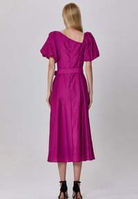 Robe fuchsia avec manches bouffantes, silhouette A-line, taille ceinturée et un léger design décolleté. Tissu lisse et léger.