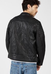 Zwarte leren jas met een geborduurde textuur op de schouders, een strak ontwerp en een getailleerde pasvorm. Draag het over een wit shirt en denim jeans.