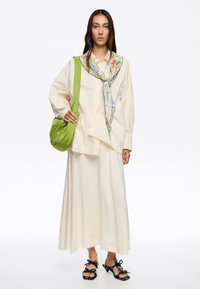 Camisa oversize crema, falda blanca con flecos, bufanda floral, bolso verde de hombro, sandalias negras con tiras retorcidas. Diseño simple y fluido.
