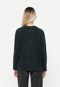 Mørk grå langermet sweatshirt med en myk tekstur og svak glans. Har rund halslinning og avslappet passform, med sidesplitt på kanten.