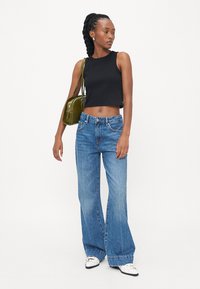 Črn skrajšan top, svetlo modri široki jeans, beli čevlji s srebrnimi detajli in mala olivno zelena torbica.