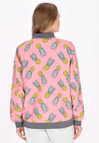 Jachetă roz cu un model de ananas și accente verzi. Gulerul și manșetele sunt gri, adăugând contrast designului vibrant.