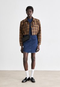Rjava karirana kratka jakna z dvema sprednjima žepoma, v kombinaciji z modrim denim mini krilom. Črna torbica preko telesa, bele nogavice in črne loafer čevlje.