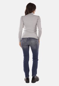 Maglione grigio a collo alto con texture a coste, abbinato a jeans skinny blu scuro con un leggero sbiadimento e tasche posteriori, indossato con scarpe nere.
