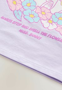 Lila Baumwoll-T-Shirt mit floralem Grafikdesign in Rosa und Blau, darunter der Text "Immer anhalten und die Blumen riechen, Miss. Bunny".