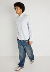 Ανοιχτό μπλε ριγέ πουκάμισο με τσέπη στο στήθος, συνδυασμένο με φαρδιά denim παντελόνια και ασημένια αθλητικά παπούτσια. Απλός σχεδιασμός, άνετη εφαρμογή.