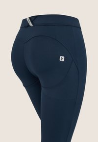 Legging laivaston sinisessä värissä, valmistettu joustavasta materiaalista, jossa on kaareva muotoilu takana, heijastava logo ja tasaiset saumat mukavuutta varten.