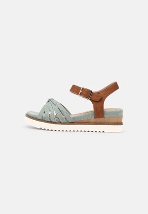 Open-toe wedge sandal with light green fabric straps, brown ankle strap with buckle, wooden heel detail, and white treaded sole.