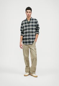 Langermet rutete skjorte i marineblå, grønn og hvit med knapper foran, kombinert med beige cargo-bukser med flere lommer og en avslappet passform.