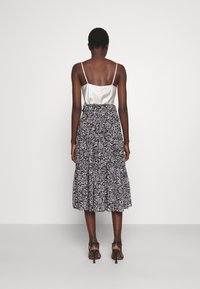 Camisole en satin avec des fines bretelles, associé à une jupe à volants à motifs floraux noirs et blancs. Le mannequin porte des sandales à talons.