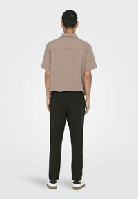 Camisa corta de manga corta en tono beige, combinada con pantalones oscuros verdes que tienen un bolsillo trasero, llevada con zapatillas blancas y negras.